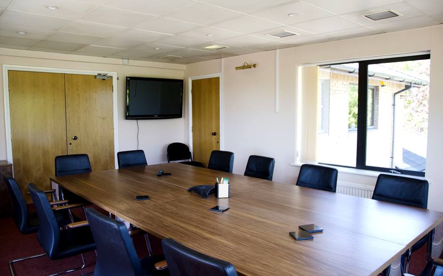 The boardroom, with a long table, twelve chairs and a wall mounted screen